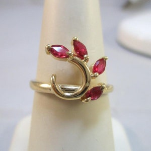 May include: A gold ring with a curved design and red gemstones. The gemstones are set in a leaf-like pattern.