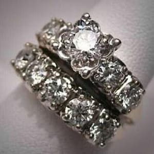 May include: A silver engagement ring set with a large, round, clear center stone and smaller, clear stones on the band. The ring is set in a floral design.