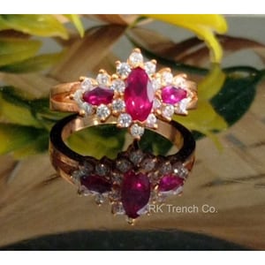 Peut inclure: Une bague en or avec un gros rubis rouge entouré de petits diamants. La bague est sertie dans un motif floral.