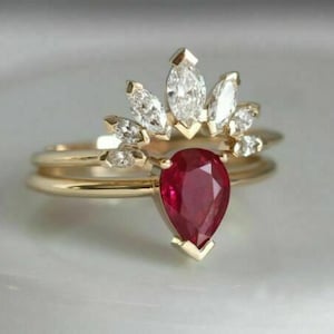 Puede incluir: Un juego de anillos de oro con una piedra preciosa roja oscura en forma de pera y una corona de diamantes talla marquesa. El anillo se asienta sobre una delicada banda de oro, mostrando un diseño clásico y elegante.