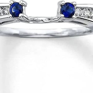 Puede incluir: Un anillo de plata con dos zafiros azules y una fila de pequeños diamantes. El anillo está diseñado para ser un realzador de banda de boda.