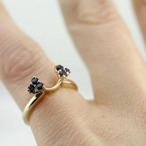 Op de afbeelding: Gouden ring met twee kleine, naar boven wijzende punten, bezet met donkerblauwe edelstenen.