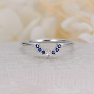 May include: A delicate silver ring with a curved row of small blue sapphires and a single, larger diamond in the center.