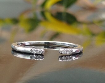 Op de afbeelding: Een zilveren ring met een opening aan één kant, met aan beide uiteinden een rij kleine, heldere diamanten.