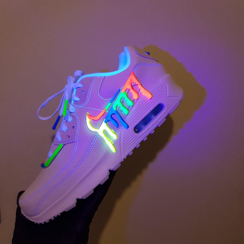 May include: A light-colored athletic shoe with neon green, orange, and blue accents. The shoe features a unique design with a dripping effect on the side and laces. The sole has a visible air pocket.