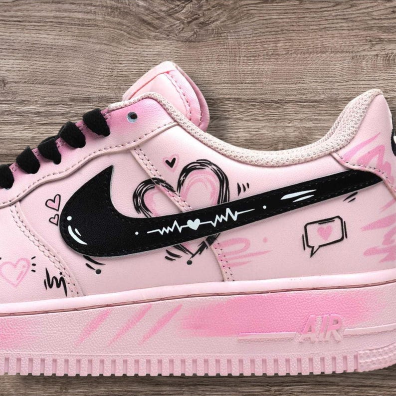 May include: Pink Air Force 1 sneakers with black accents and heart-themed illustrations. The sneakers feature a black Nike swoosh, black laces, and a pink sole. The design includes hearts, speech bubbles, and a heartbeat line.