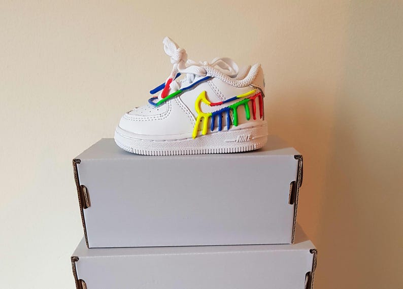 Puede incluir: Zapatillas blancas de cuero con un dise&ntilde;o de salpicaduras de pintura de colores en el lateral. Las zapatillas est&aacute;n encima de dos cajas blancas.