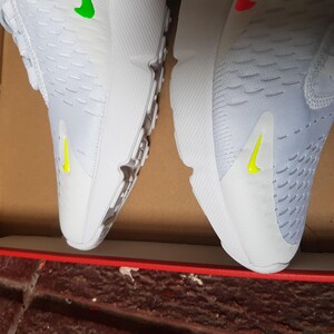 May include: Pair of white athletic shoes with a textured design. The shoes have a yellow swoosh logo on the side and a green accent on the top. The soles are gray and white.