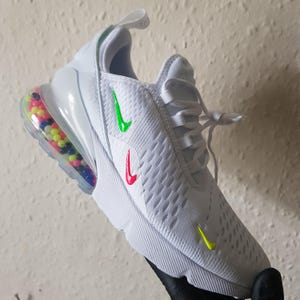 May include: White athletic shoe with a colorful bubble-filled heel and a white sole. The shoe features a green, red, and yellow swoosh logo. The shoe is a size 9.