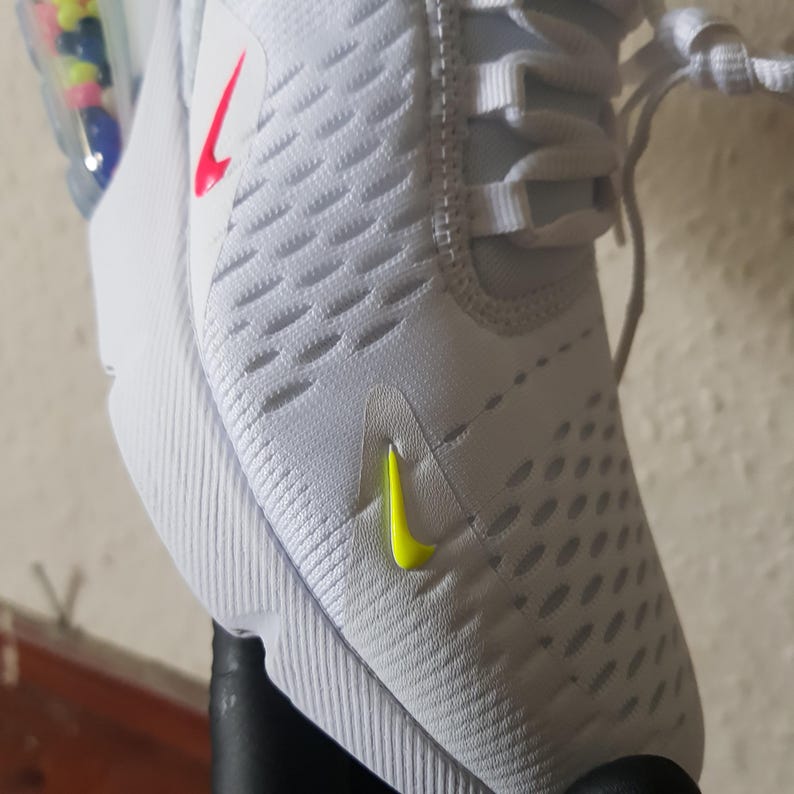 May include: White athletic shoe with a textured upper. Features a neon yellow swoosh logo on the side and a red swoosh logo on the upper. The shoe has white laces and a white sole.