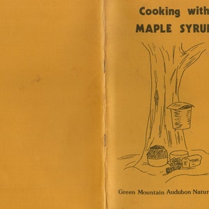 May include: An open booklet with a mustard-yellow cover featuring a black illustration of a tree with a maple syrup collection system. The text "Cooking with Maple Syrup" is at the top, and "Green Mountain Audubon Nature Center" is at the bottom.