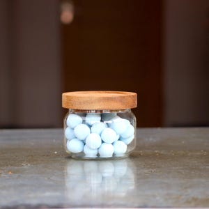 Könnte beinhalten: Ein Glasgefäß mit einem Holzdeckel gefüllt mit hellblauen Bonbons.