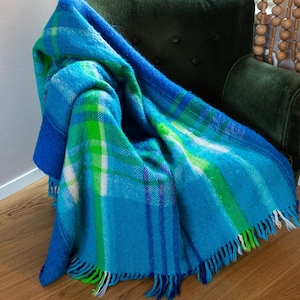 May include: A blue and green plaid throw blanket with white accents and fringe. The blanket is folded and draped over a green armchair.