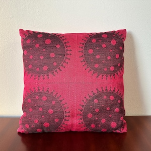 Puede incluir: Una almohada roja con un patrón geométrico negro de círculos y puntos. La almohada está hecha de una tela suave y texturizada.