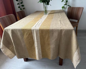 May include: A rectangular beige linen tablecloth with vertical stripes in yellow and white. The tablecloth is draped over a wooden table. The room has two chairs with woven backs and a vase of flowers.