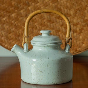 May include: A white ceramic teapot with a speckled glaze and a bamboo handle. The teapot has a lid and a spout.