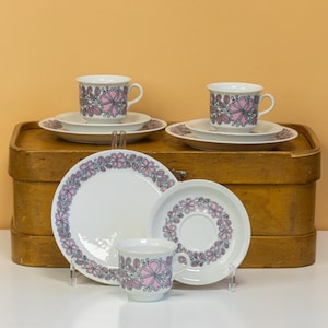 Puede incluir: Juego de cuatro tazas de té y platillos con estampado floral rosa y gris. Las tazas y los platillos tienen un fondo blanco con un diseño floral rosa y gris.