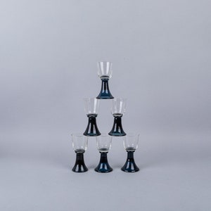 May include: Set of six clear glass shot glasses with dark blue bases stacked in a pyramid shape.