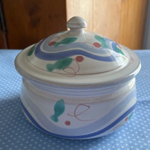 May include: A white ceramic serving dish with a lid. The dish has a blue, green, and red abstract design with wavy lines and small circles.