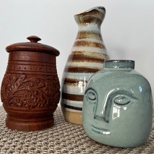 May include: Three ceramic vases, one with a brown and white striped design, one with a carved wooden design, and one with a blue face design.