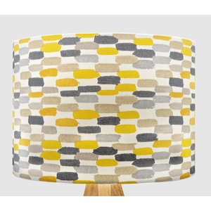 May include: A yellow, grey, and beige patterned lampshade with a geometric design. The lampshade is made of fabric and has a cylindrical shape.