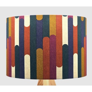 May include: A cylindrical lampshade with a geometric pattern in shades of orange, red, purple, blue, and cream. The pattern features vertical stripes with rounded shapes.