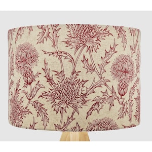 May include: A beige lampshade with a red floral pattern of stylised thistles. The lampshade is cylindrical and has a smooth, linen-like texture.