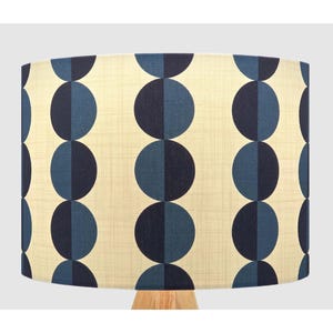 May include: A cylindrical lampshade featuring a repeating pattern of vertical columns of circles. Each circle is split into two halves, one in dark navy blue and the other in a lighter blue shade, set against a textured cream-coloured background.