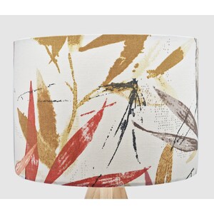 May include: A white lampshade with a red, brown and black abstract leaf pattern.