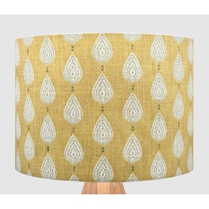 May include: A cylindrical drum lampshade featuring a mustard yellow fabric base with a repeating pattern of white teardrop shapes. Each teardrop contains intricate white line details and is vertically aligned with small dark green accents.