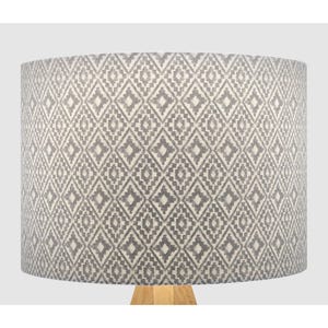 May include: A white lampshade with a grey geometric pattern. The lampshade is cylindrical and has a smooth surface.