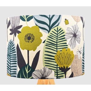 May include: A lampshade with a floral pattern featuring yellow flowers, green leaves, and a white background. The lampshade is made of fabric and has a cylindrical shape.