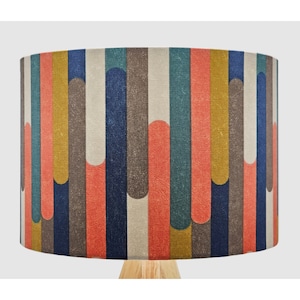 May include: A cylindrical lampshade featuring a geometric pattern of vertical stripes in shades of blue, red, yellow, and brown. The stripes are interrupted by curved shapes in a contrasting colour.