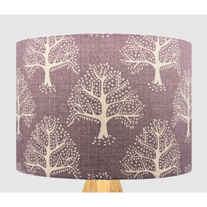 May include: A cylindrical lampshade featuring a repeating pattern of cream-coloured trees on a textured, muted purple background. The fabric has a visible weave, and the design shows multiple stylised trees with detailed branches and leaves.
