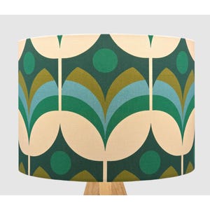 May include: A cylindrical lampshade featuring a repeating geometric pattern of stylised floral shapes and circles. The design incorporates a colour palette of dark forest green, olive green, light blue, and cream, printed on a textured fabric surface.