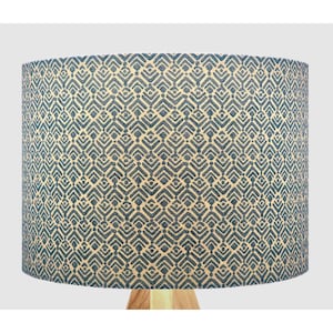 May include: A cylindrical lampshade featuring a repeating geometric pattern of dark blue chevron shapes and small dots set against a light beige background. The design covers the entire exterior surface of the drum-shaped shade.