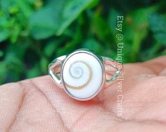 May include: A silver ring with a white and brown seashell inlay. The seashell has a spiral pattern.