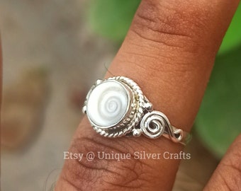 May include: A silver ring with a white shell cabochon set in a twisted rope design. The ring has a delicate, swirling design on the band. Etsy @ Unique Silver Crafts