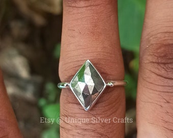 Puede incluir: Anillo de plata con una piedra de pirita en forma de diamante. La pirita tiene una superficie metálica y reflectante. El anillo se muestra en un dedo. El nombre de la tienda Etsy "Unique Silver Crafts" es visible.