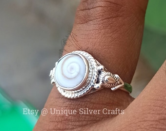 May include: A silver ring with a white shell stone featuring a spiral pattern. The ring has a decorative design on the band. Etsy @ Unique Silver Crafts.