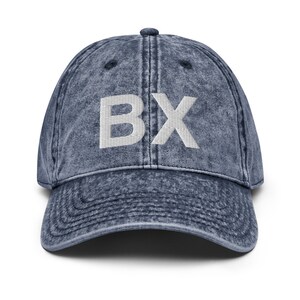 Puede incluir: Una gorra de béisbol de mezclilla azul con las letras "BX" bordadas en blanco en la parte delantera.