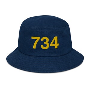 Pode incluir: Um chapéu de pescador azul marinho com o número 734 bordado em amarelo na frente.