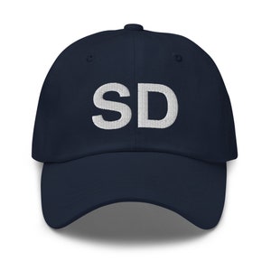 Peut inclure: Une casquette de baseball bleu marine avec un "SD" brodé en blanc sur le devant.
