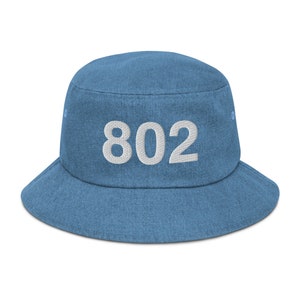 May include: A blue denim bucket hat with white embroidered text that reads "802".