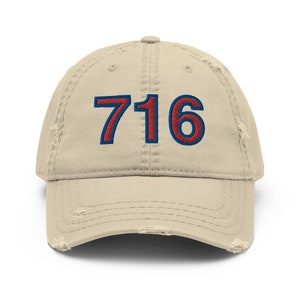 Op de afbeelding: Een beige, verweerde baseballpet met het nummer 716 geborduurd in rood met een blauwe omtrek.