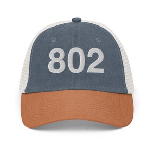 May include: A blue and brown trucker hat with a white mesh back. The hat has the number "802" embroidered on the front in white.