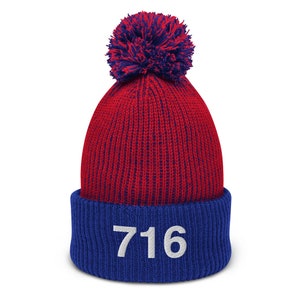 May include: Red and blue knit beanie with a white pom pom on top. The beanie has a blue cuff with the number "716" embroidered in white.
