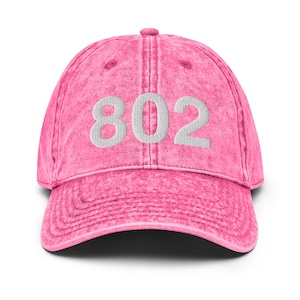 May include: Pink denim baseball cap with white embroidered text "802" on the front.
