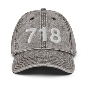 May include: A gray distressed denim baseball cap with the number 718 embroidered in white on the front.
