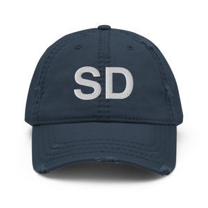 Peut inclure: Une casquette de baseball en denim bleu marine usée avec les lettres "SD" brodées en blanc sur le devant.